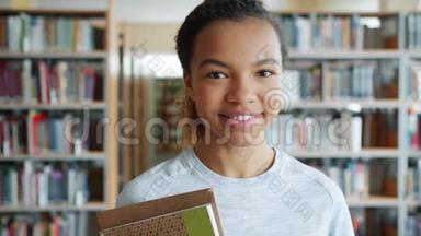 富有魅力的非裔美国学生在图书馆捧着书微笑的画像